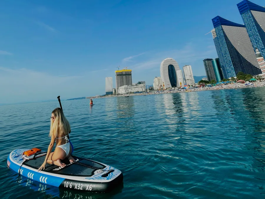 A woman on a SUP board in the sea off Batumi, high-rises on the shore