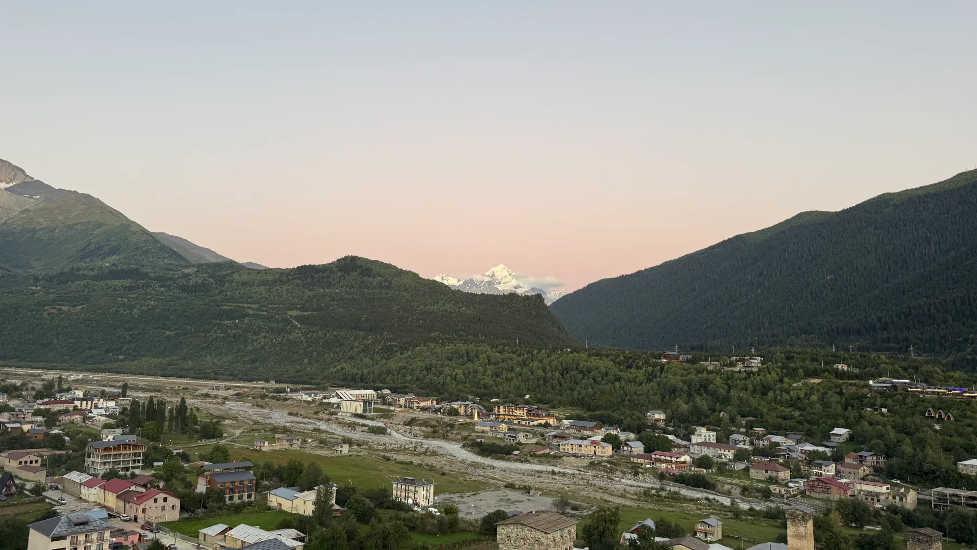 Mestia from above in pink twilight: houses, a Svan tower and a distant snowy peak