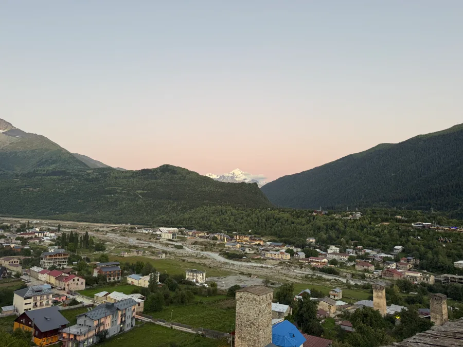 Mestia from above in pink twilight: houses, a Svan tower and a distant snowy peak
