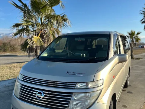 Серебристый минивэн Nissan Elgrand спереди, на стоянке среди пальм