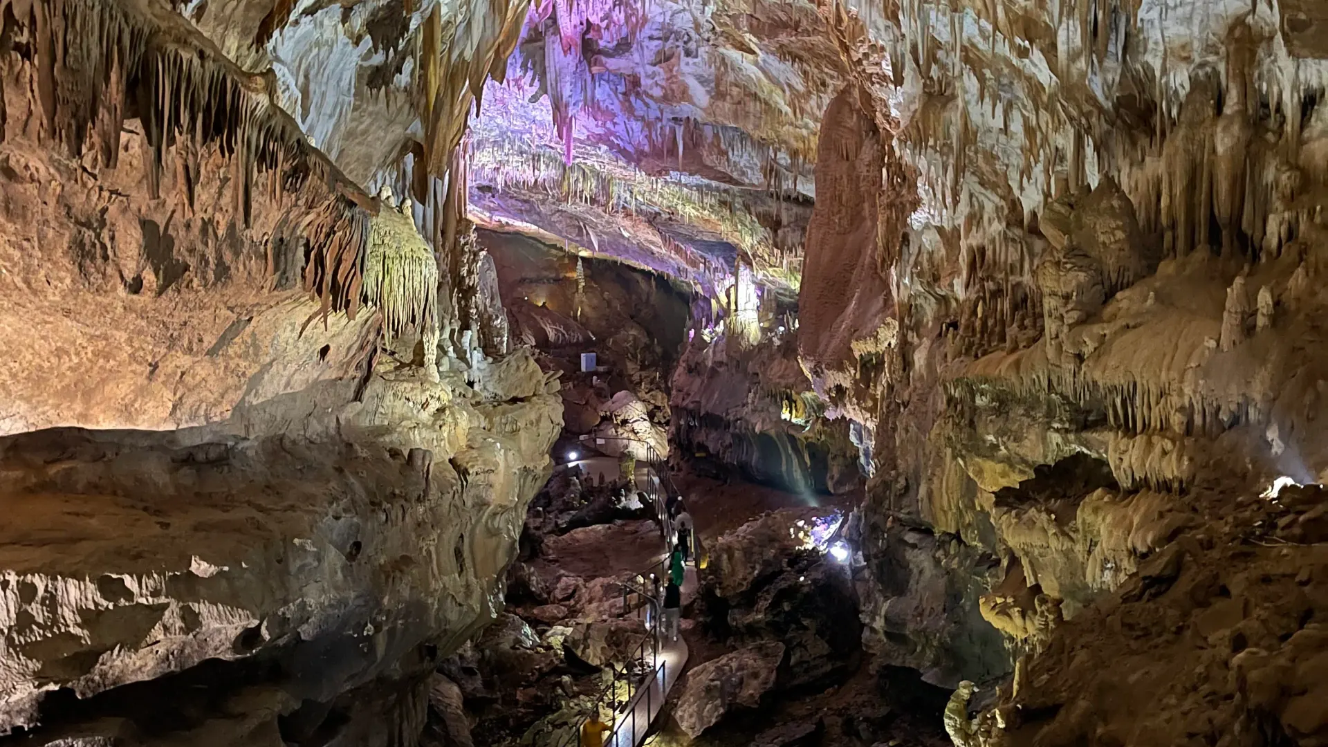 Lit-up hall of Prometheus Cave with stalactites and a visitor walkway