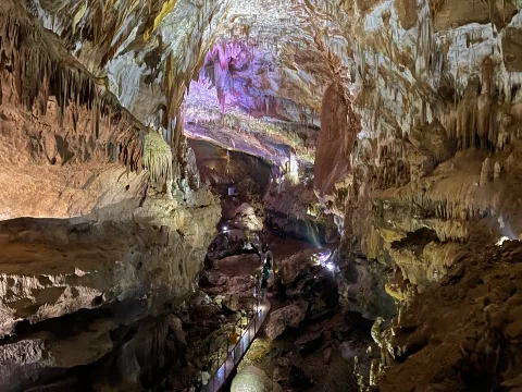 Lit-up hall of Prometheus Cave with stalactites and a visitor walkway
